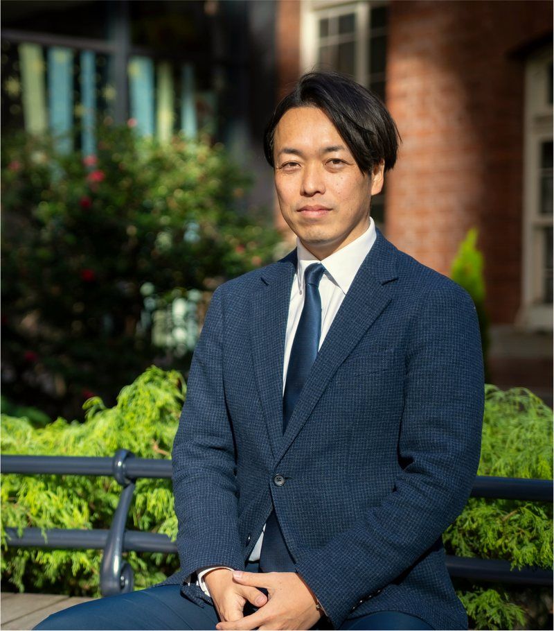 青いジャケット姿で座る井上浩之の写真